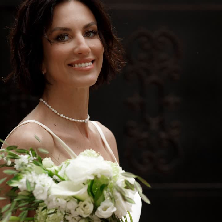 Novia sonriente con vestido de seda y ramo blanco