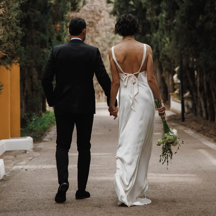 Novios paseando de espaldas; ella lleva un vestido de seda con la espalda abierta