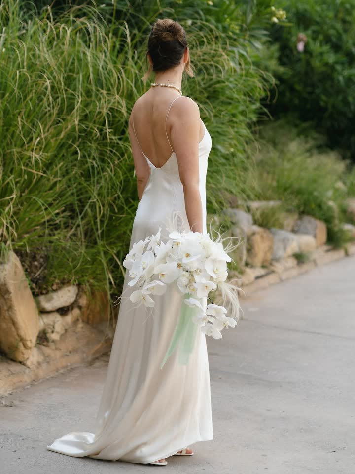 Novia de espaldas con vestido de seda escotado y orquídeas blancas entre la vegetación