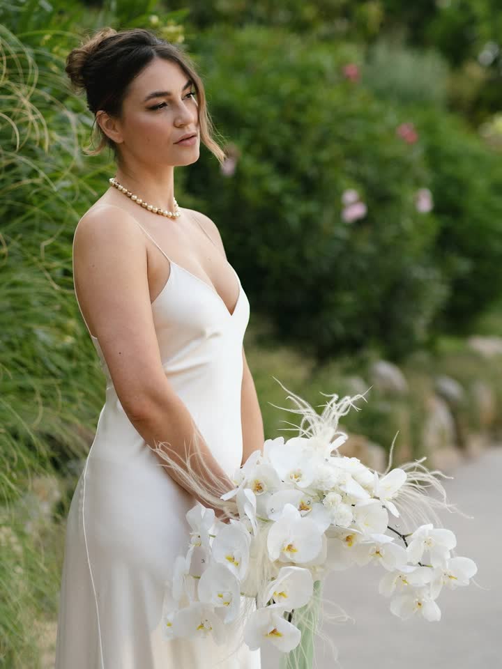 Novia con vestido lencero de seda, collar de perlas y orquídeas en un jardín