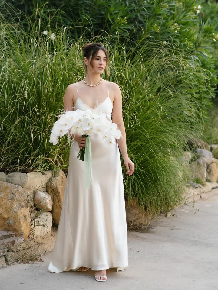 Novia de cuerpo entero con vestido de seda y orquídeas entre hierbas altas