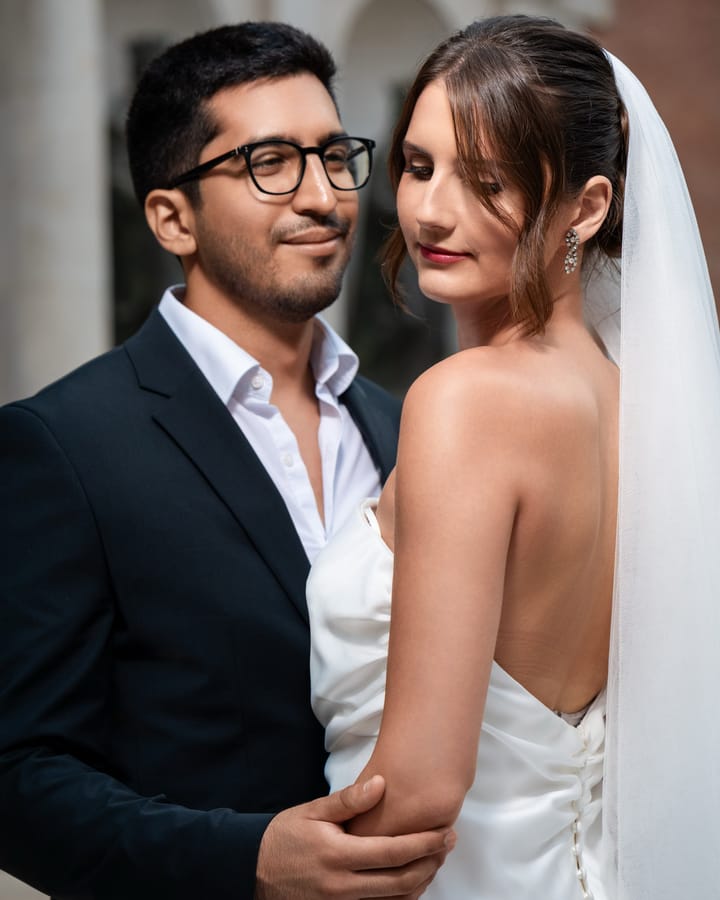Novia de perfil con vestido de espalda abierta, abrazada al novio